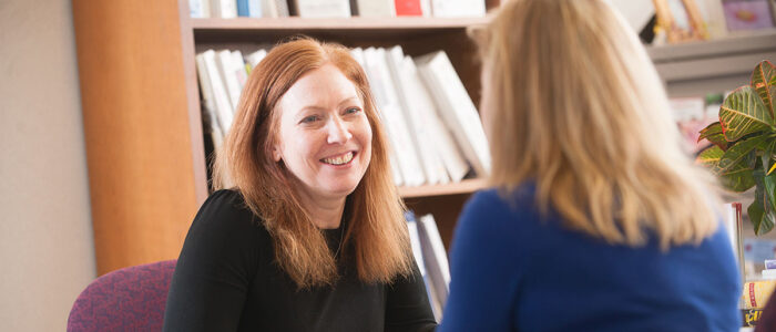 Two women talking in front of a bookshelf