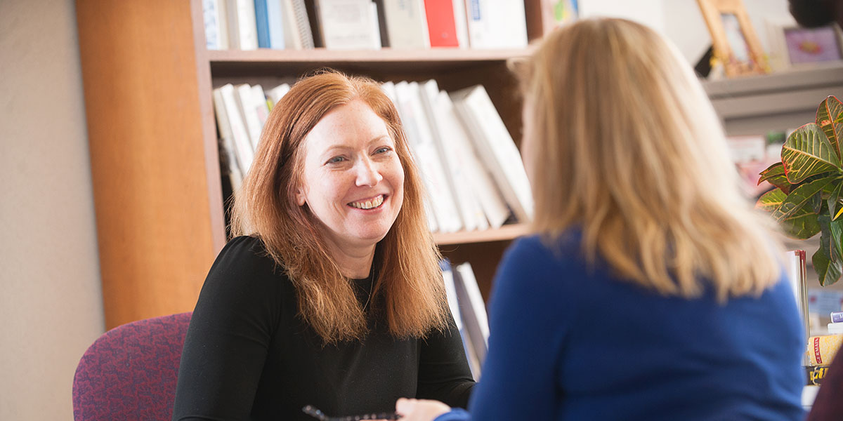 Two women talking in front of a bookshelf