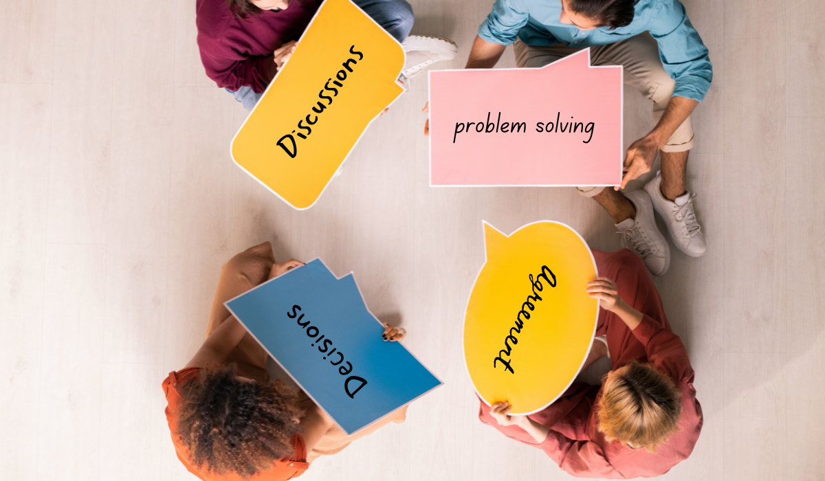 four people sitting on the floor holding signs with words: discussion, problem solving, decisions, agreement