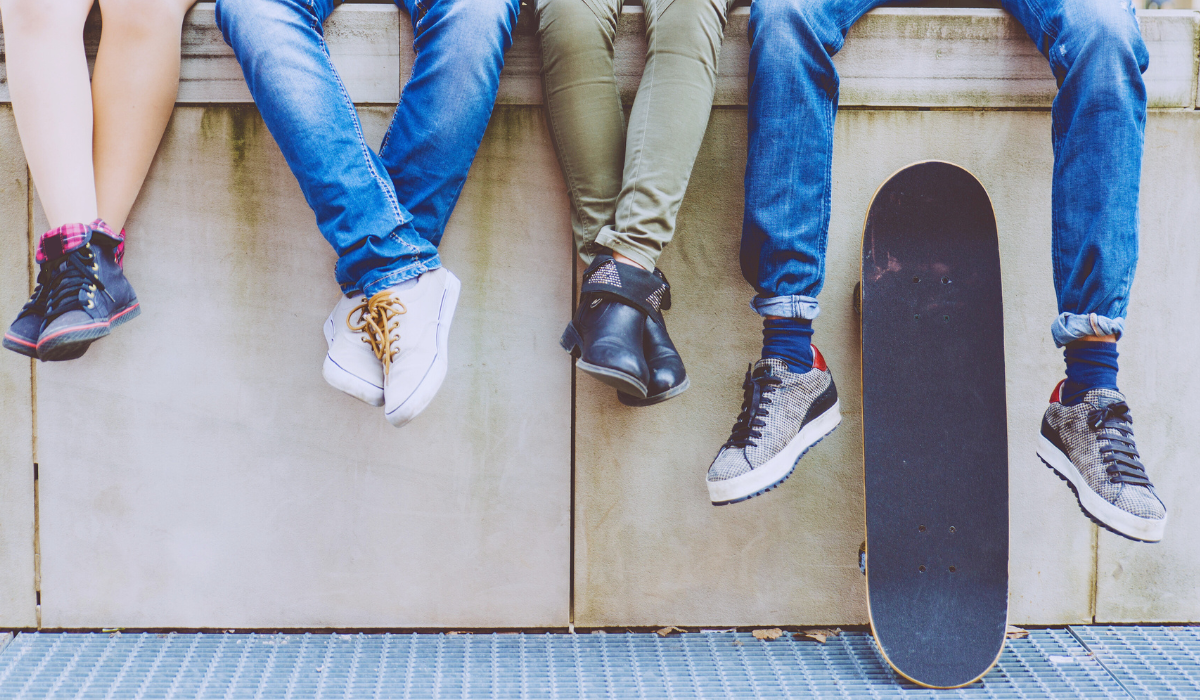 a photo showing just the legs and feet of several teens sitting on wall