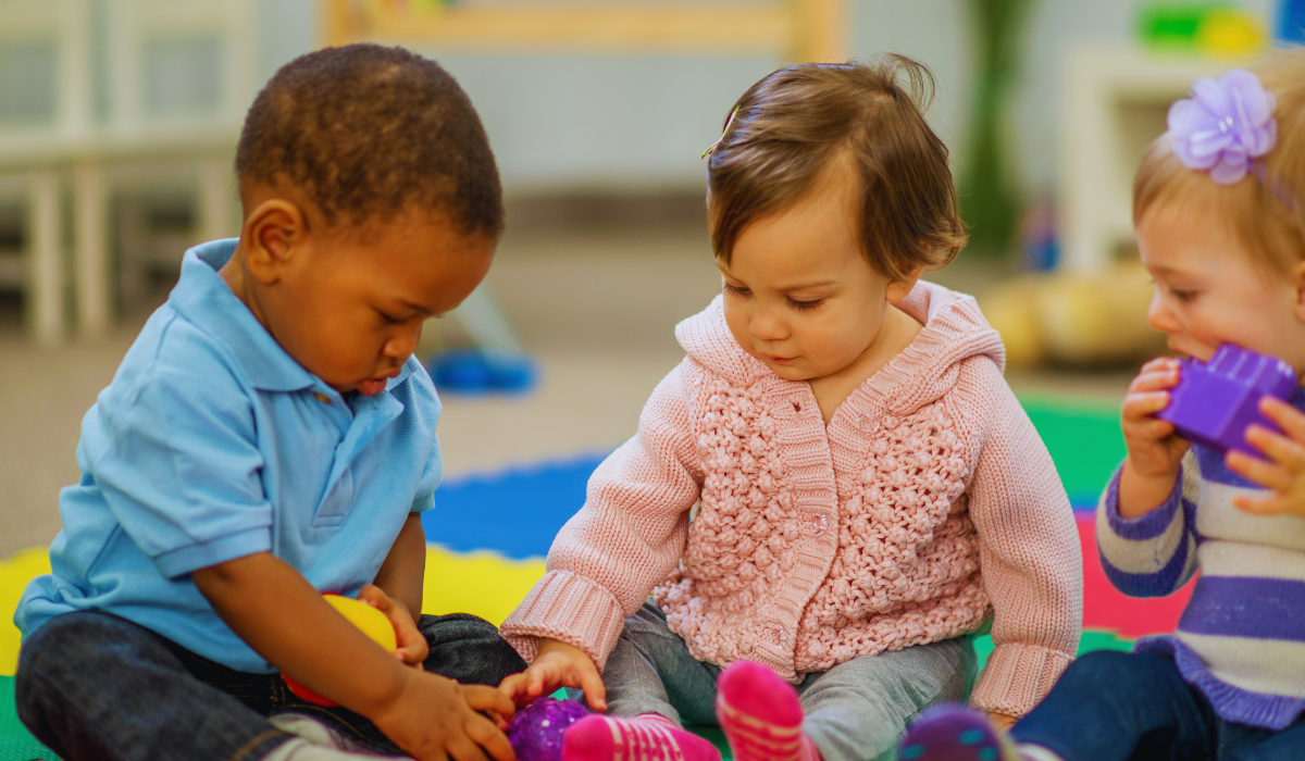 toddler boy and toddler girl in bright clothes reaching for a toy