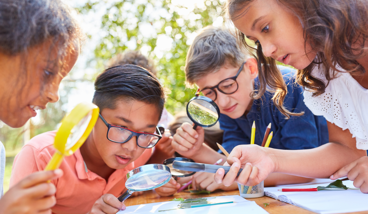 4 kids outside looking at a paper through magnifying glass