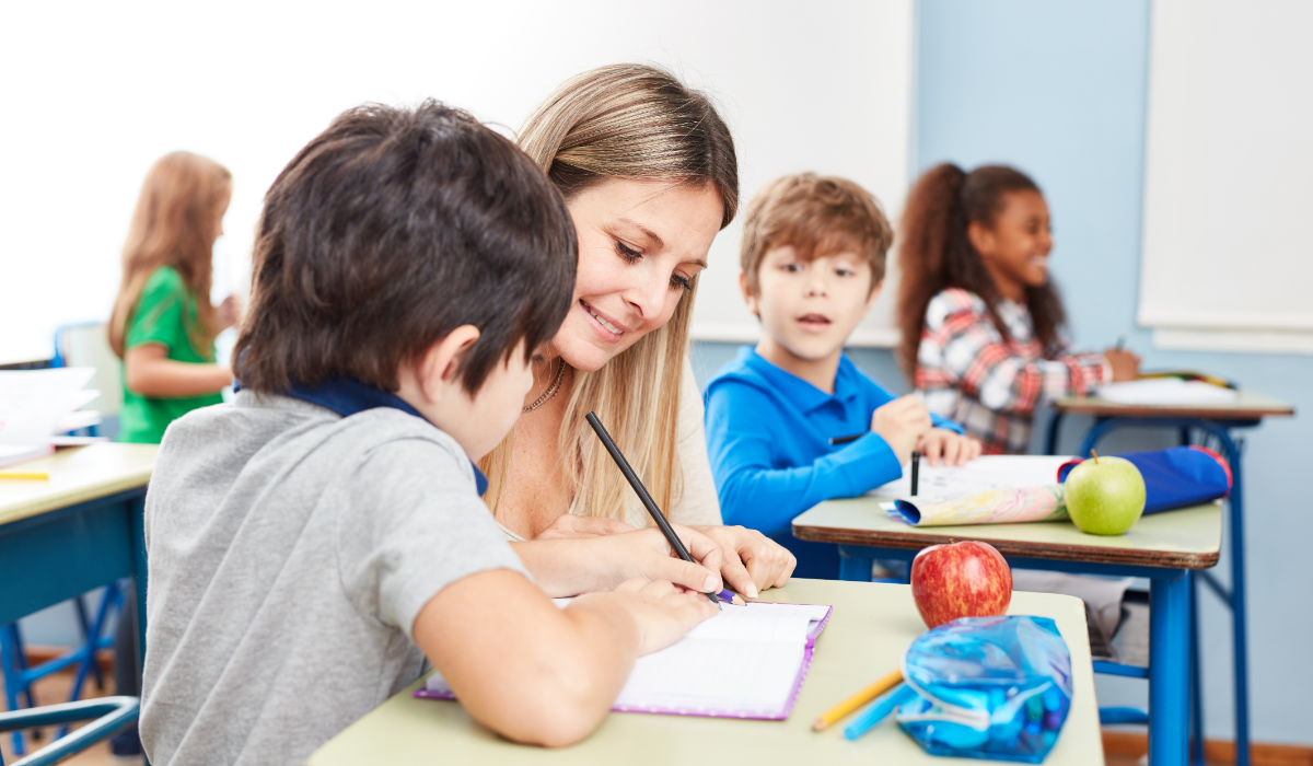 adult assisting a student at his desk in the classroom