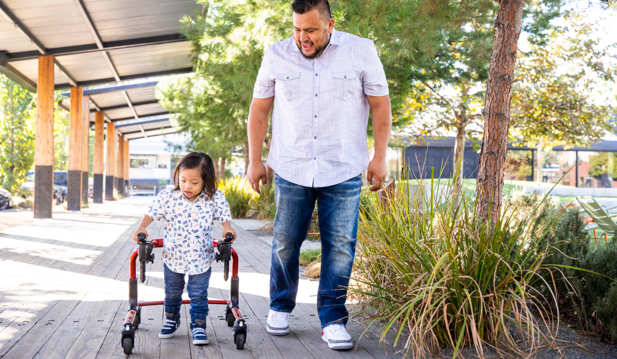 young Hispanic boy walks using a walker with his dad