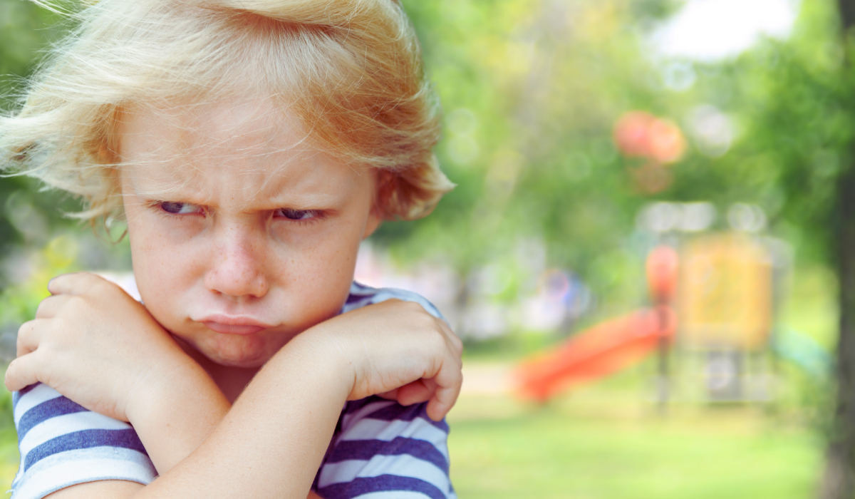 upset annoyed child with arms crossed near a playground with slides