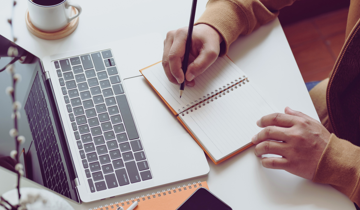 photo of laptop and person taking notes on a notepad