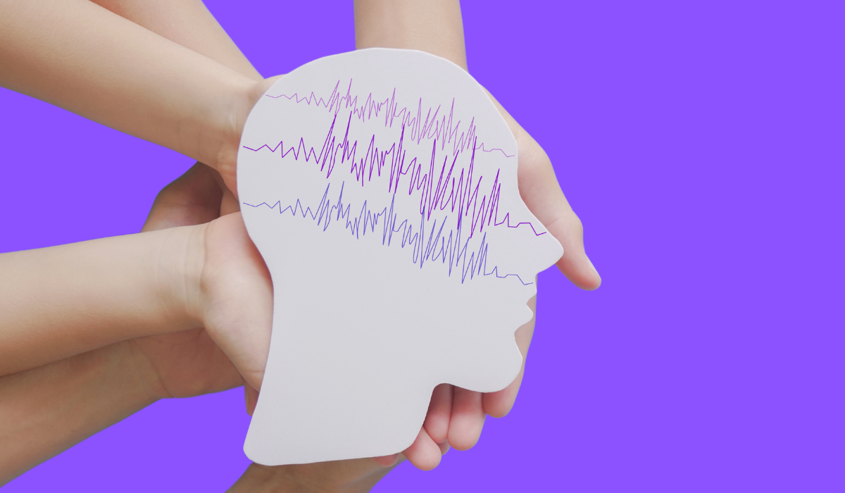 hands holding a cutout of a head shape with brain wave lines drawn